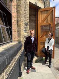 Two people stood outside bar venue with old brick wall and wooden door